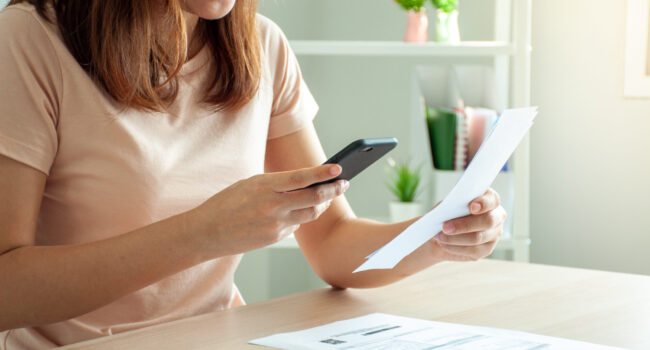 A woman uses a smartphone to scan the barcode to pay monthly phone bills after receiving an invoice sent to home. Online bill payment concept